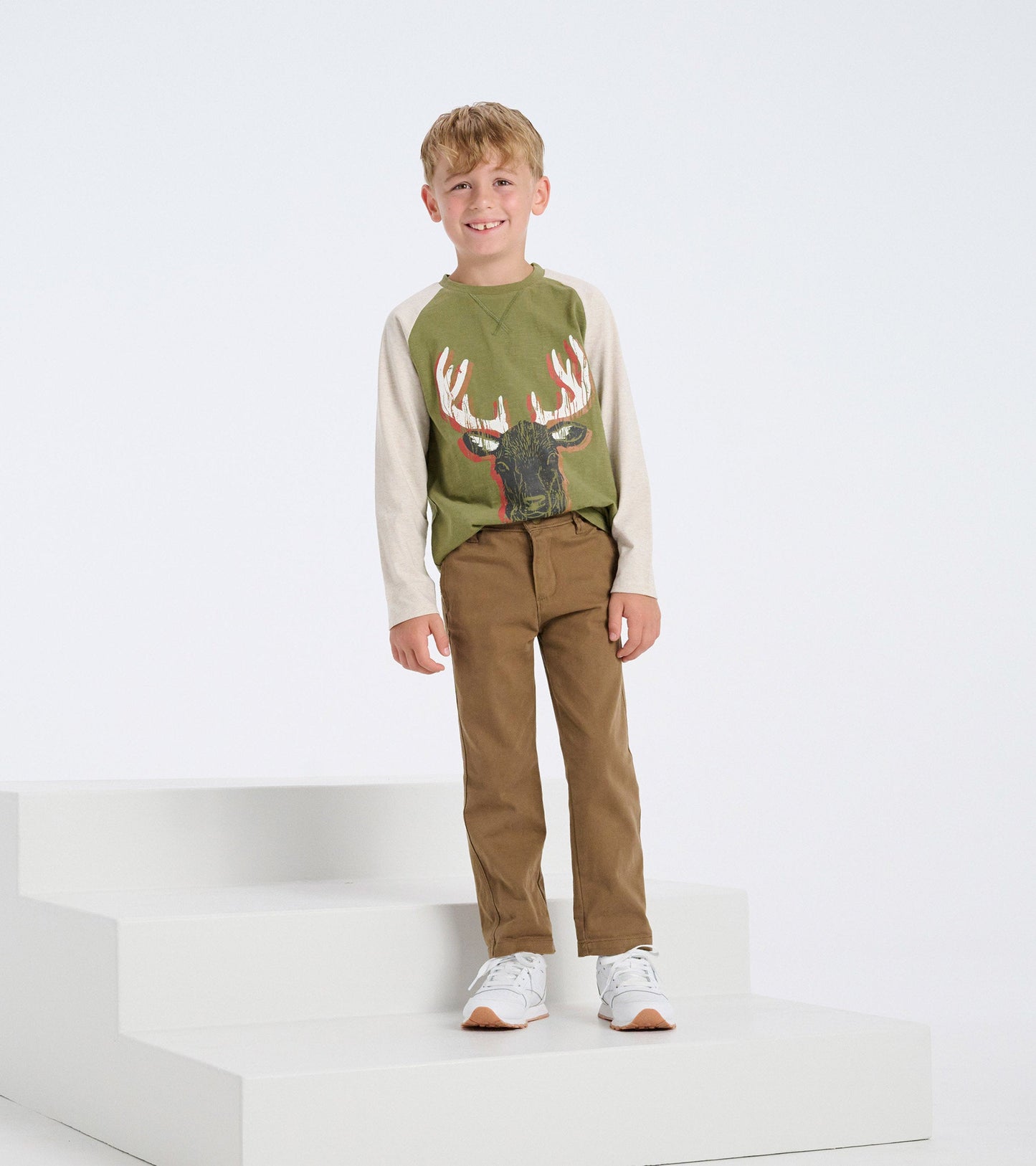 Long sleeve green t-shirt with a moose graphic, paired with brown pants, worn by a smiling boy standing on steps.