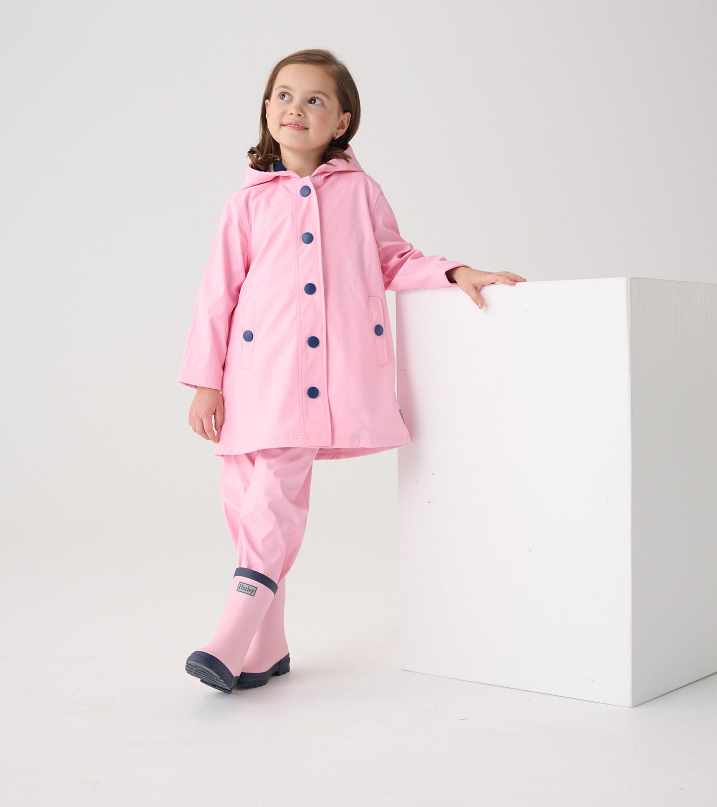 Pink button-up raincoat with navy buttons and hood, paired with matching pink rain pants and boots.