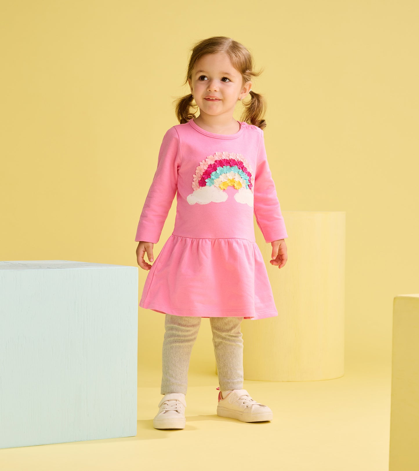 Toddler girl wearing a pink long-sleeve dress with rainbow cloud applique and flared skirt, front view