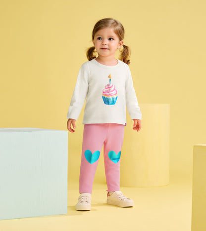Long-sleeve cream t-shirt with cupcake graphic paired with pink leggings featuring blue heart patches.