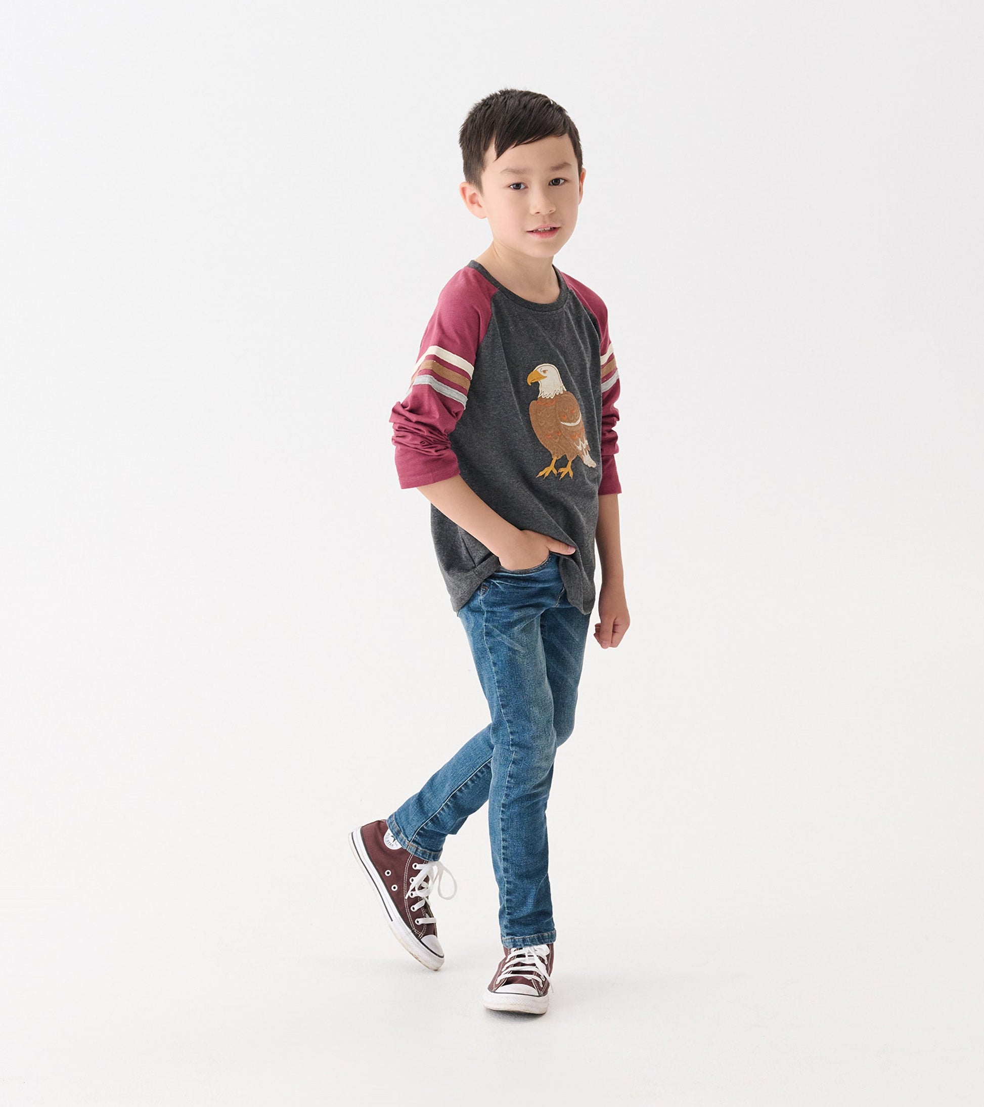 Gray long sleeve raglan t-shirt with maroon sleeves and eagle graphic, worn by a boy with blue jeans and sneakers.