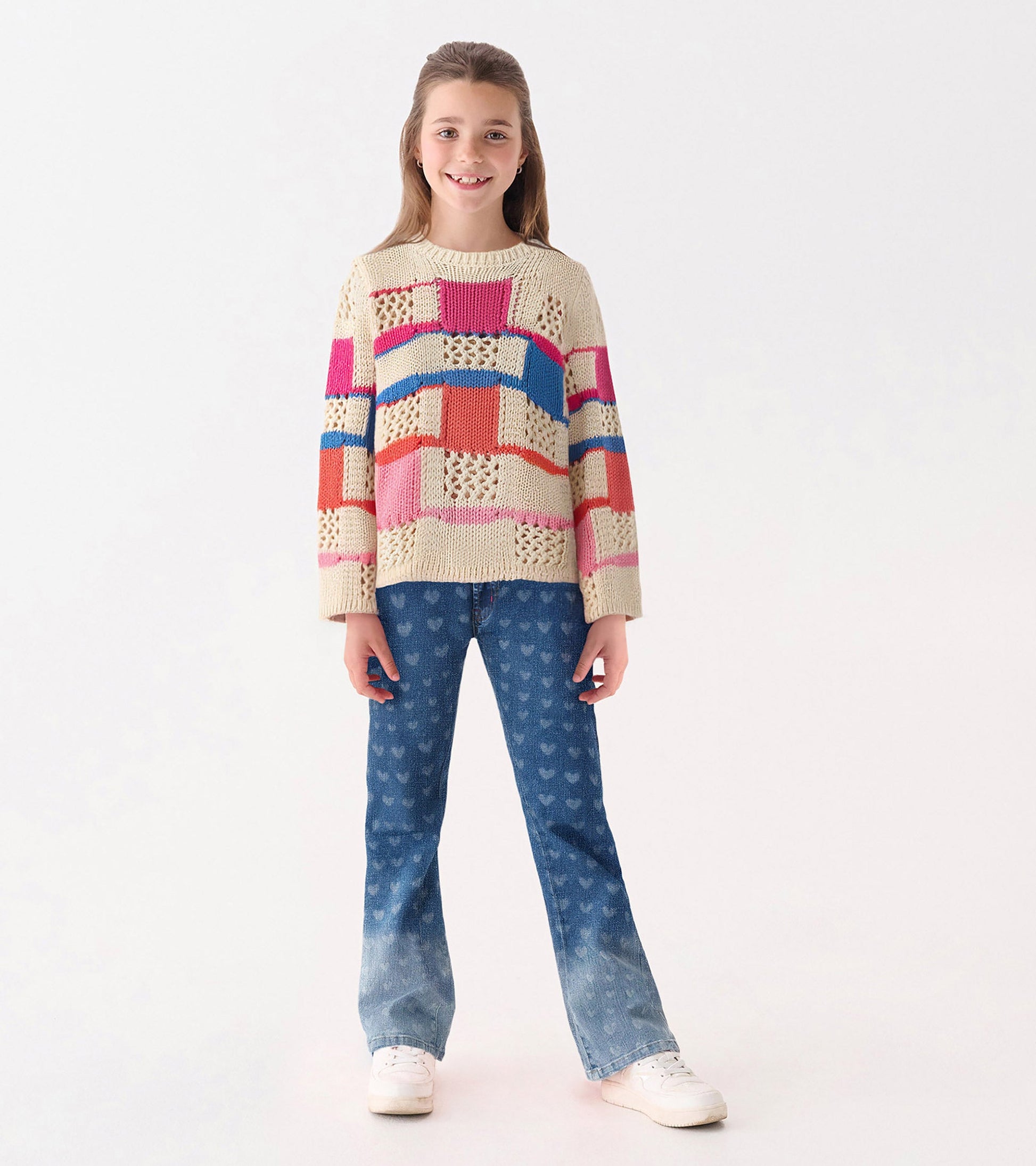 Knit sweater featuring a mix of colorful patches in pink, blue, and orange, paired with heart-patterned jeans.
