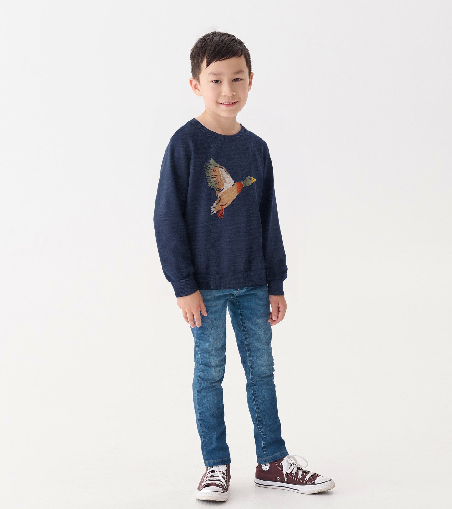 Navy crew neck sweater featuring a colorful duck design, worn by a boy with blue jeans and sneakers.