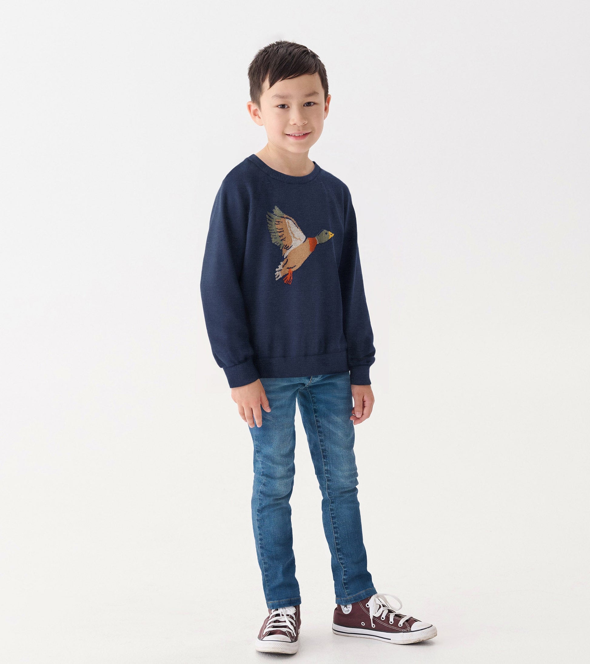 Navy crew neck sweater featuring a colorful duck design, worn by a boy with blue jeans and sneakers.