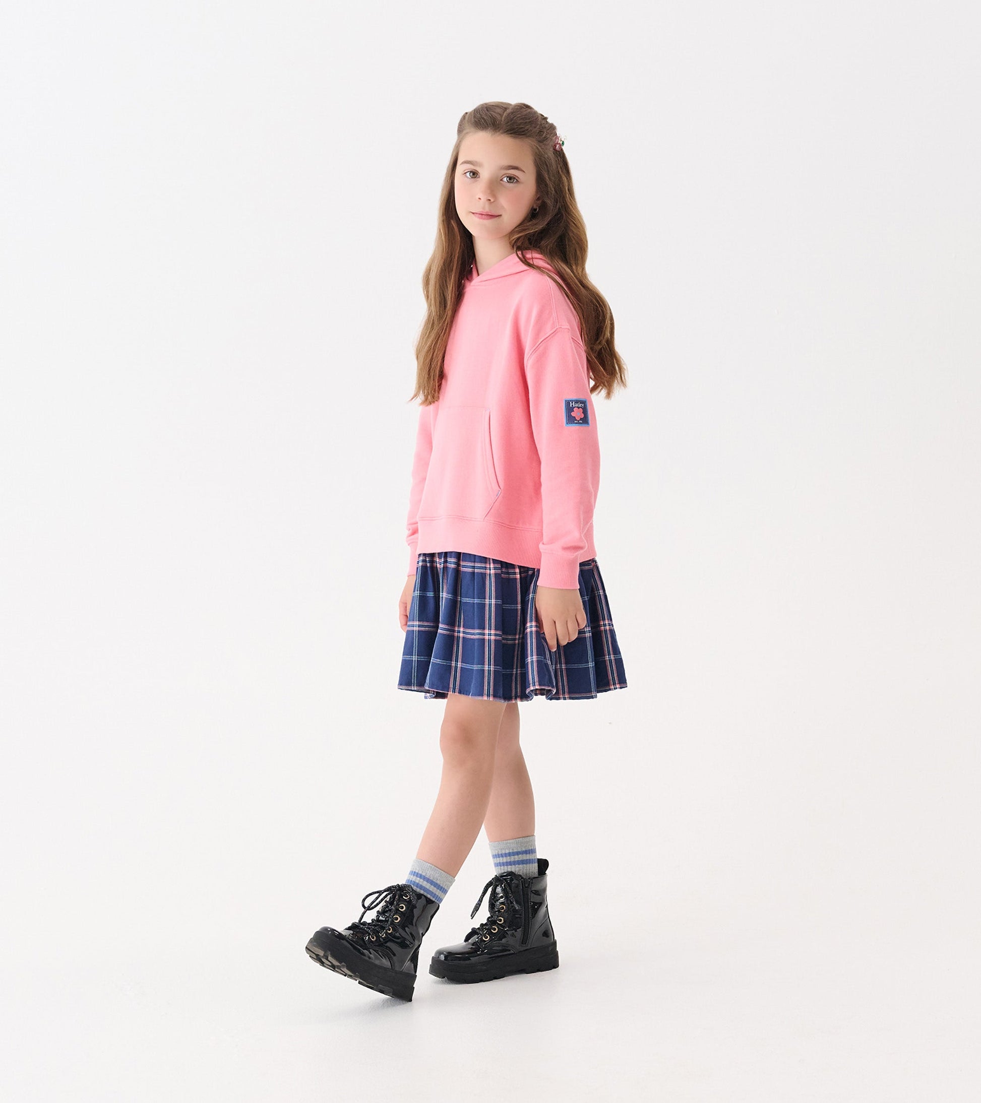 Pink hoodie paired with a navy plaid skirt, worn with black boots and striped socks.