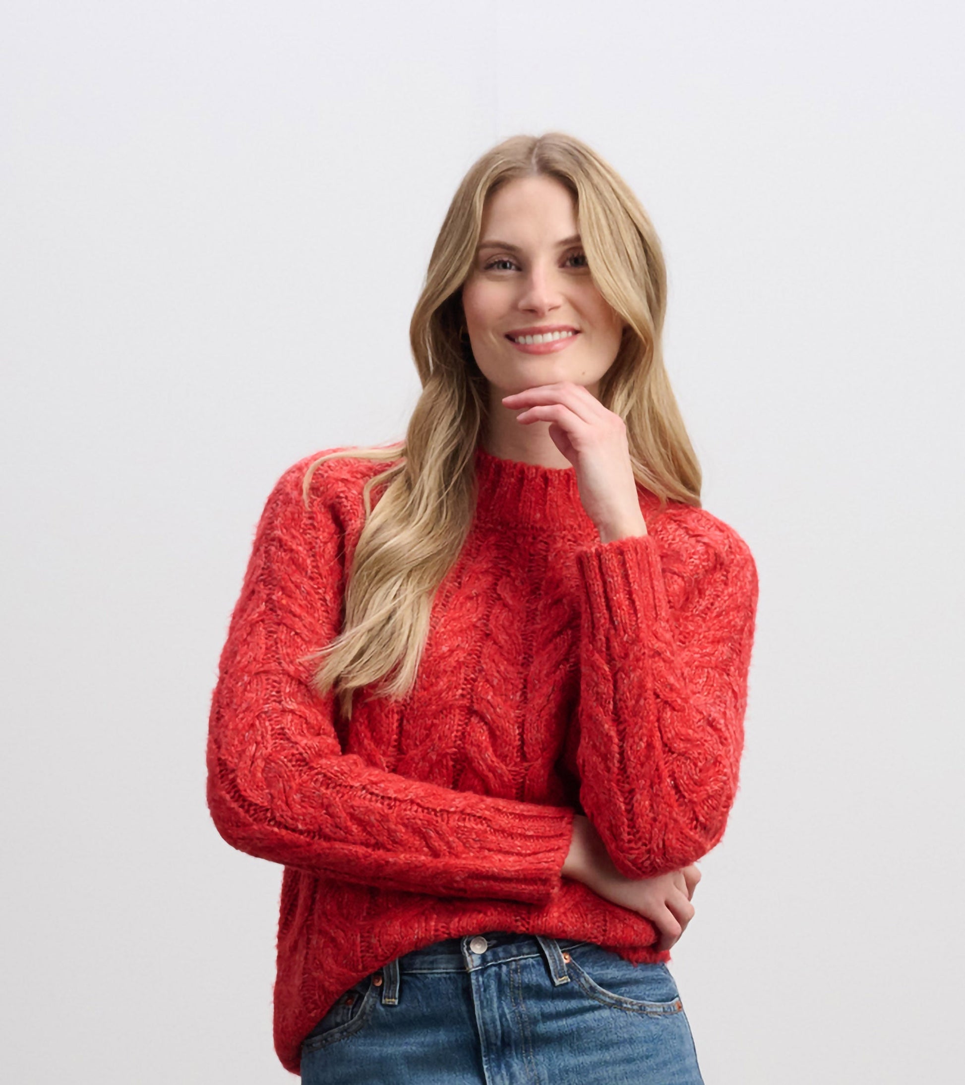 Red cable knit jumper with a round neckline and long sleeves, styled with casual denim jeans.