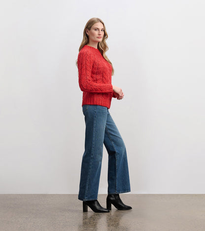 Red cable knit jumper with long sleeves, styled with blue jeans and black heeled boots, shown from the side.