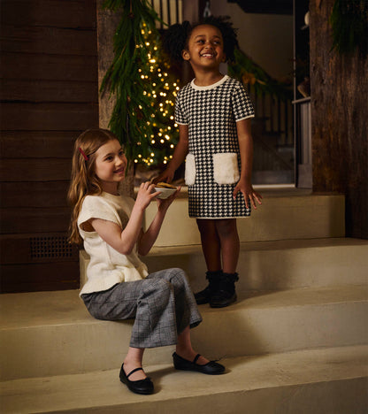 Girls black-and-white houndstooth sweater dress with short sleeves and faux fur patch pockets, front view