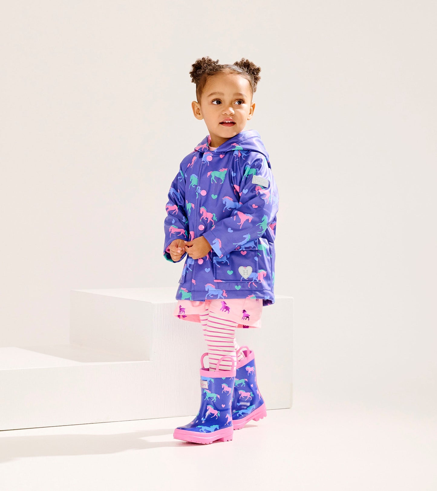 Purple button-up raincoat with horse and heart patterns, paired with pink striped leggings and matching rain boots.
