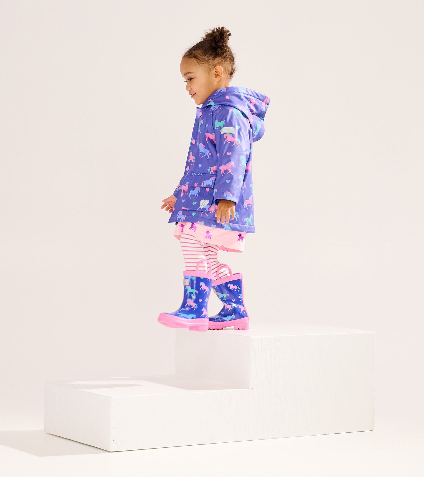 Purple raincoat with horse and heart patterns, paired with striped leggings and matching rain boots, worn by a young girl.