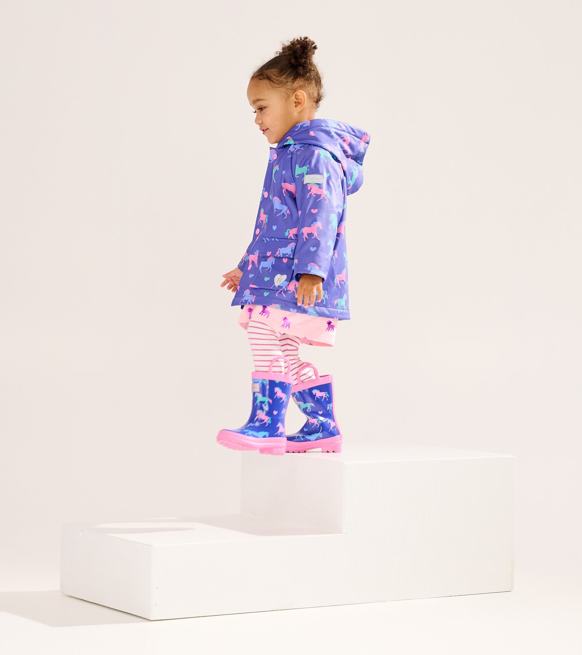 Purple raincoat with horse and heart patterns, paired with striped leggings and matching rain boots, worn by a young girl.
