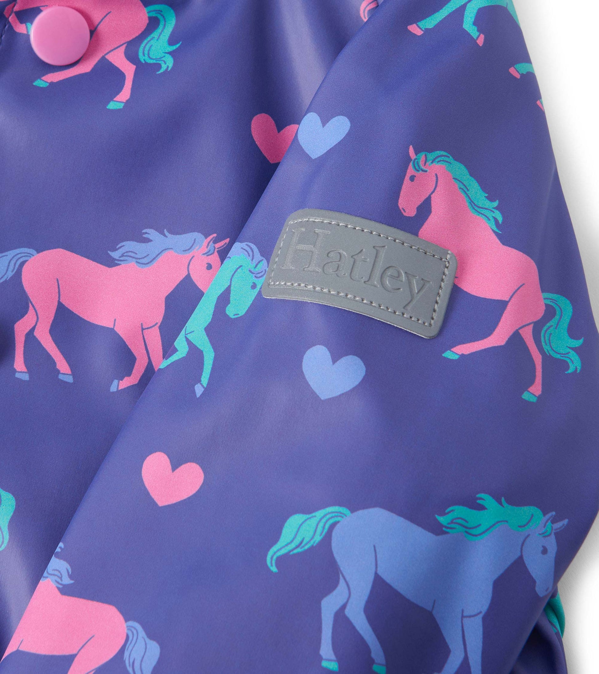 Purple raincoat featuring pink and blue horses and hearts, with a button closure and a textured patch.