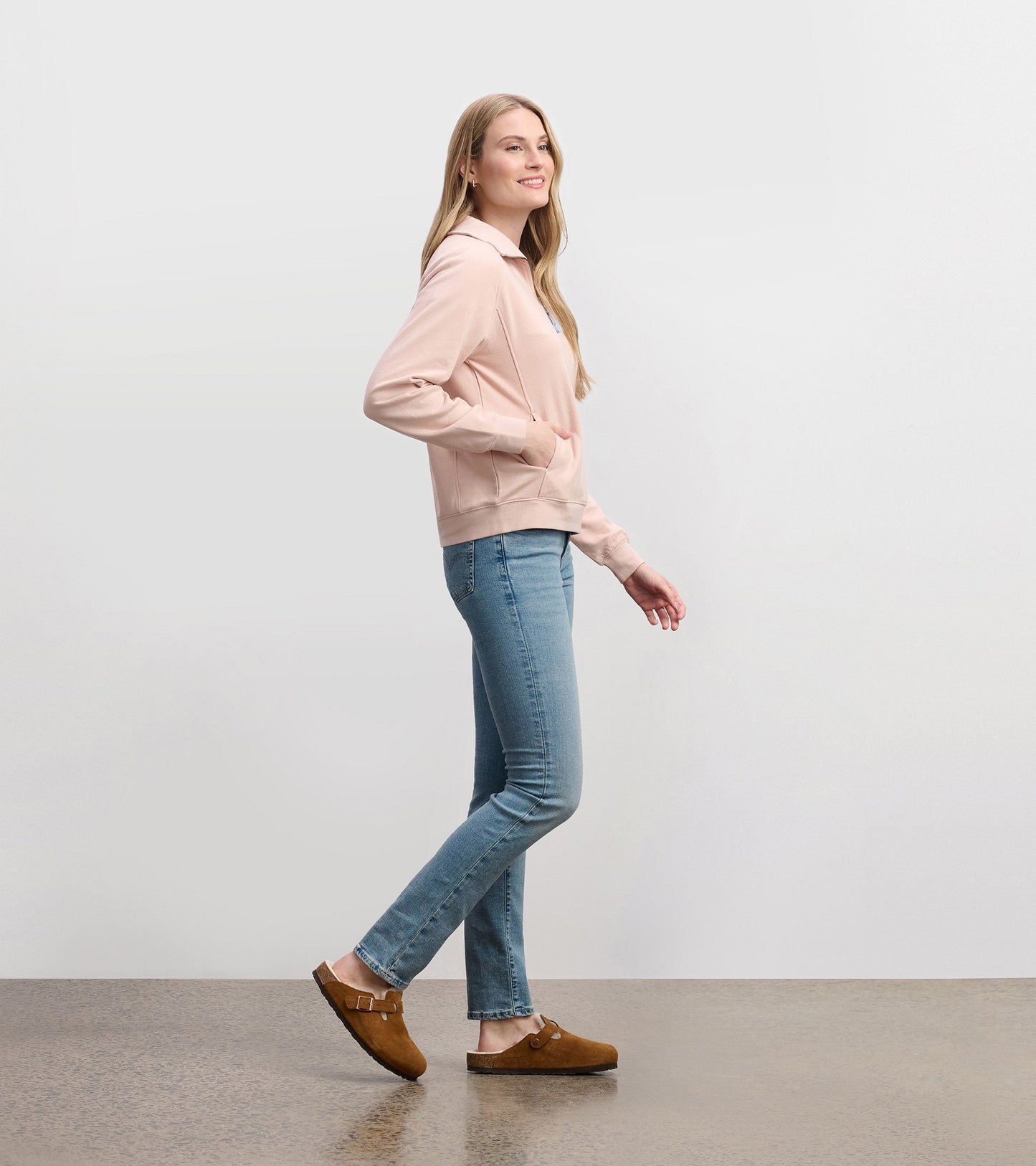 Pink mock neck pullover with long sleeves and front pockets, paired with light blue jeans and brown clogs, shown from the si…