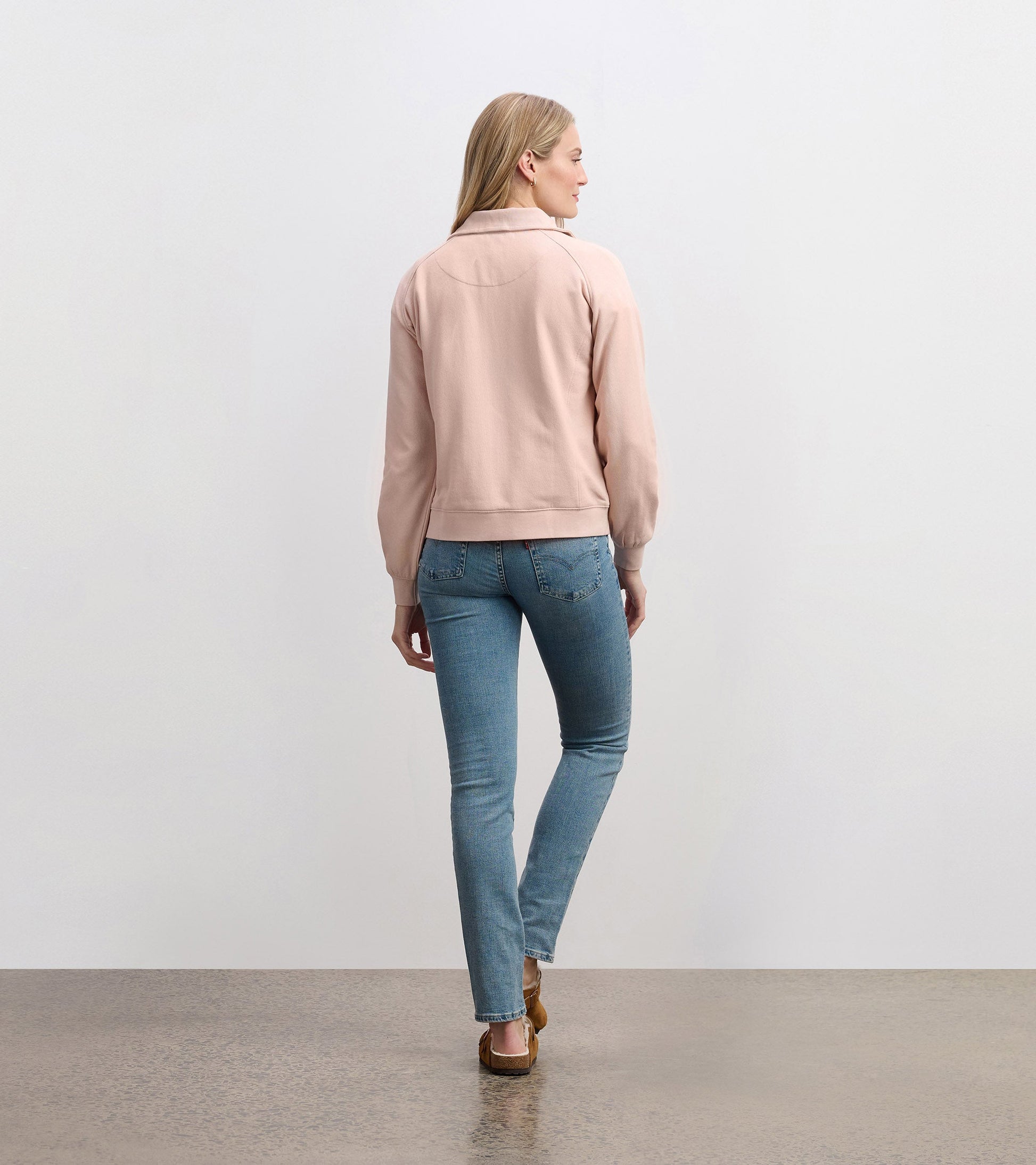 Pink mock neck pullover with long sleeves, viewed from the back, paired with light blue jeans.