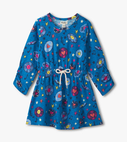 Blue cinched waist dress featuring a colorful music-themed print with records, stars, and musical notes. Long sleeves.