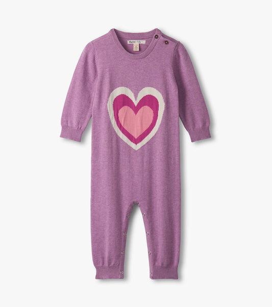 Purple sweater romper featuring a large heart design in pink shades, with snap closures at the bottom and button details on…