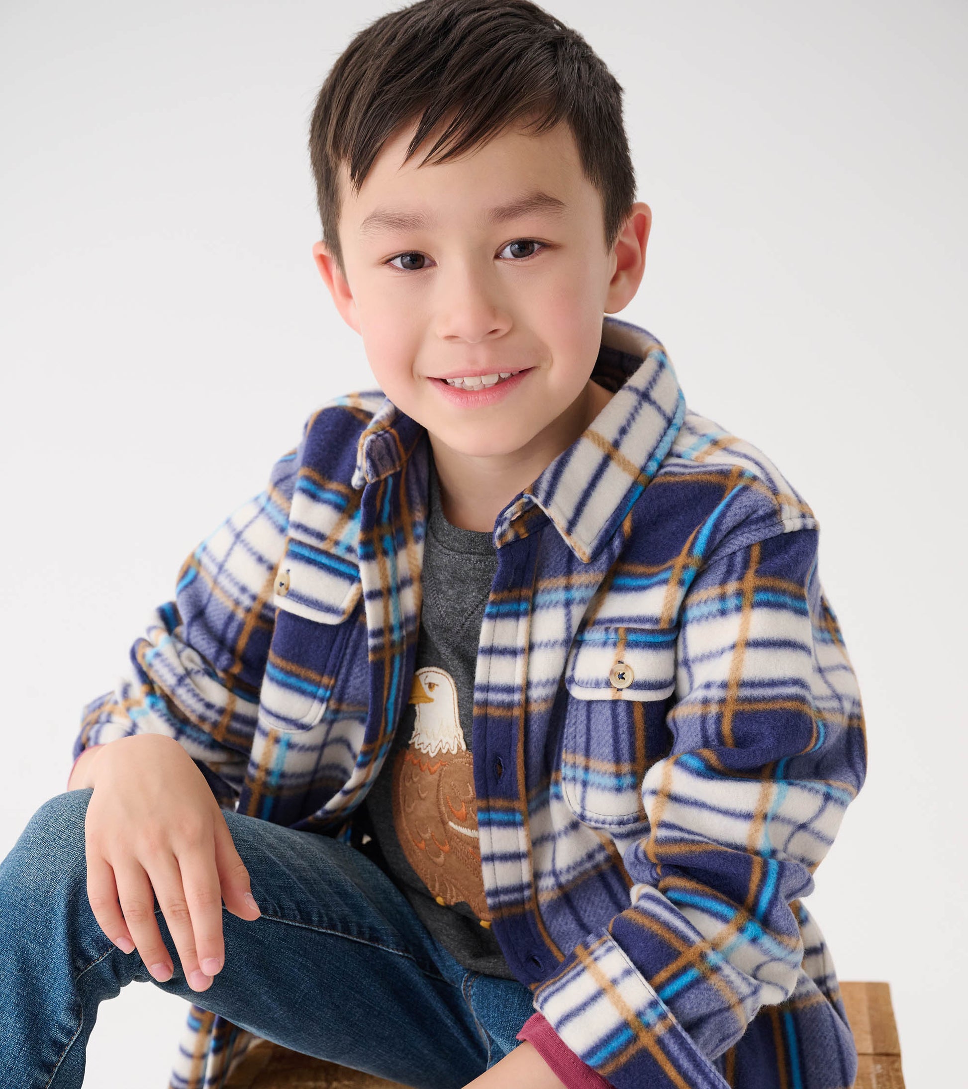 Plaid fleece button-up shirt in blue, white, and brown, featuring two chest pockets, worn by a boy sitting casually.