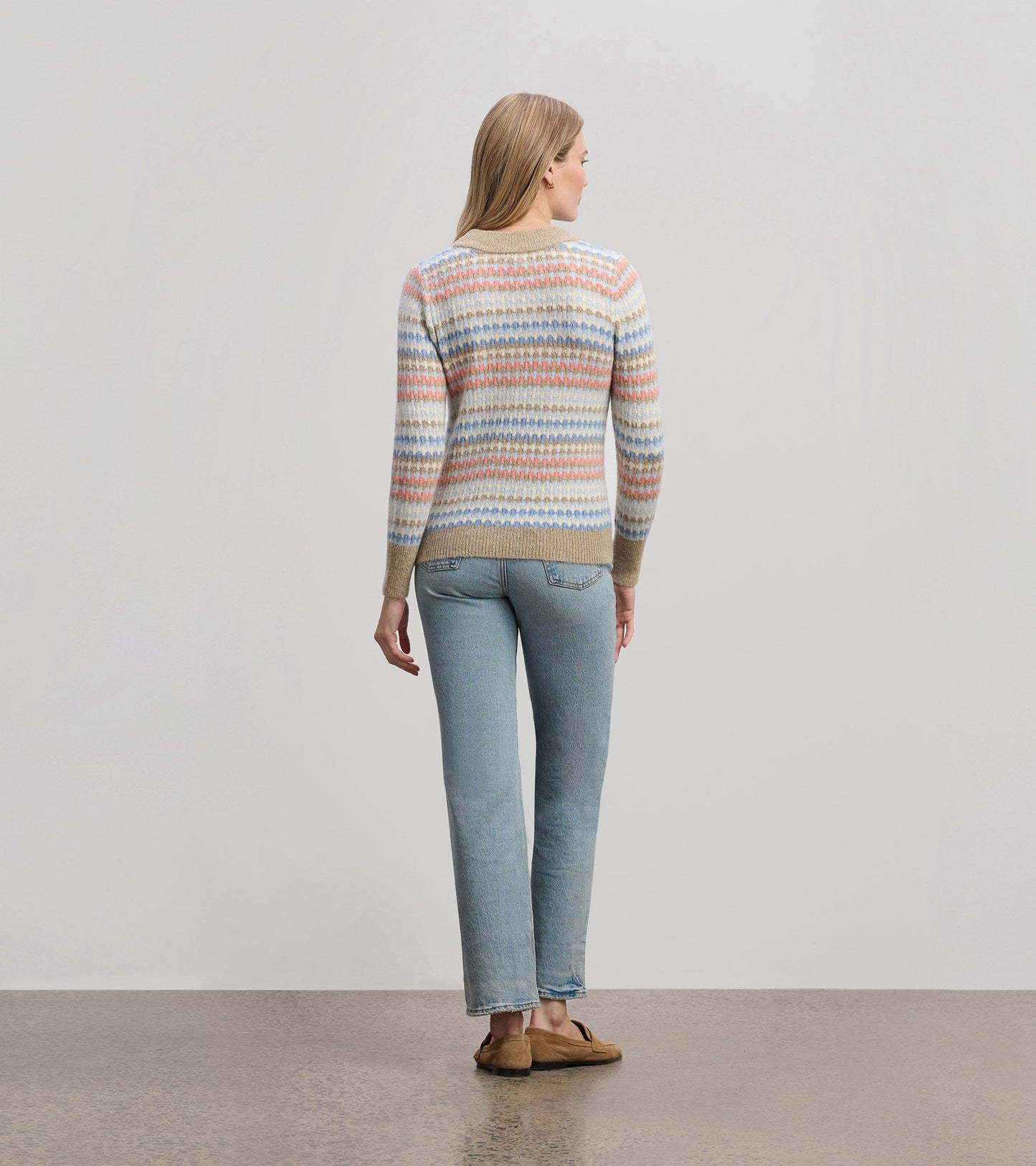 Back view of a cozy, multicolored striped jumper in soft knit fabric, paired with light blue jeans.