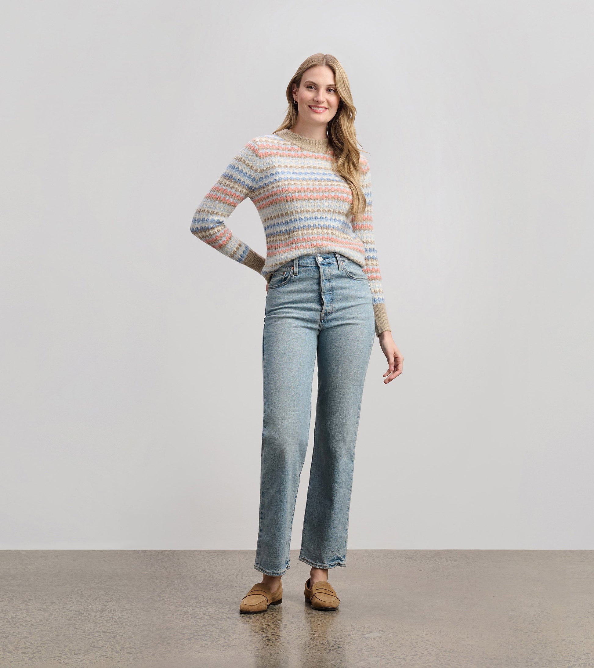 Multicolored striped jumper with long sleeves, paired with light blue jeans and loafers, styled casually.