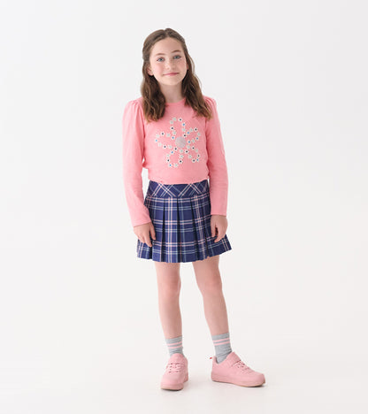 Navy plaid pleated skirt paired with a pink long-sleeve top, worn by a girl standing against a white background.