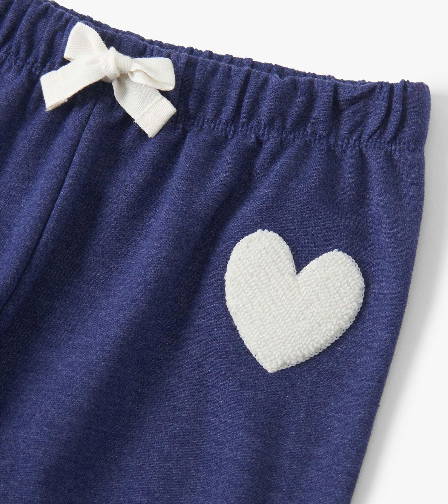 Patriot blue baggy track pants with a white heart patch and a bow detail on the elastic waistband.