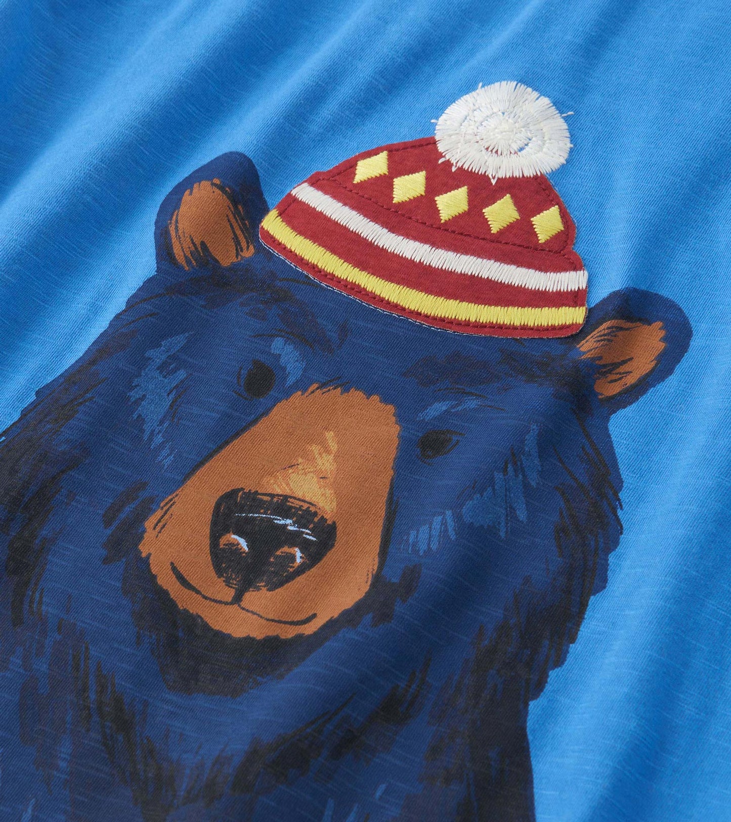 Blue long sleeve tee featuring a graphic of a bear wearing a red and yellow hat with a pom-pom.