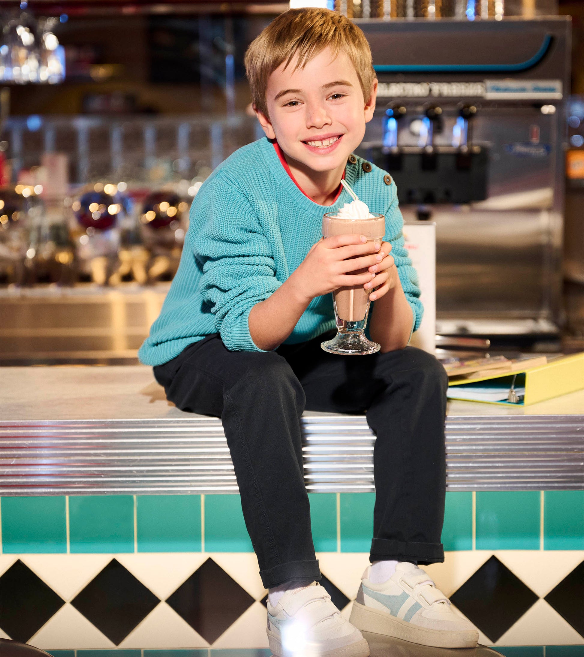 Teal button neck sweater with textured knit, worn by a boy sitting and holding a milkshake in a diner setting.
