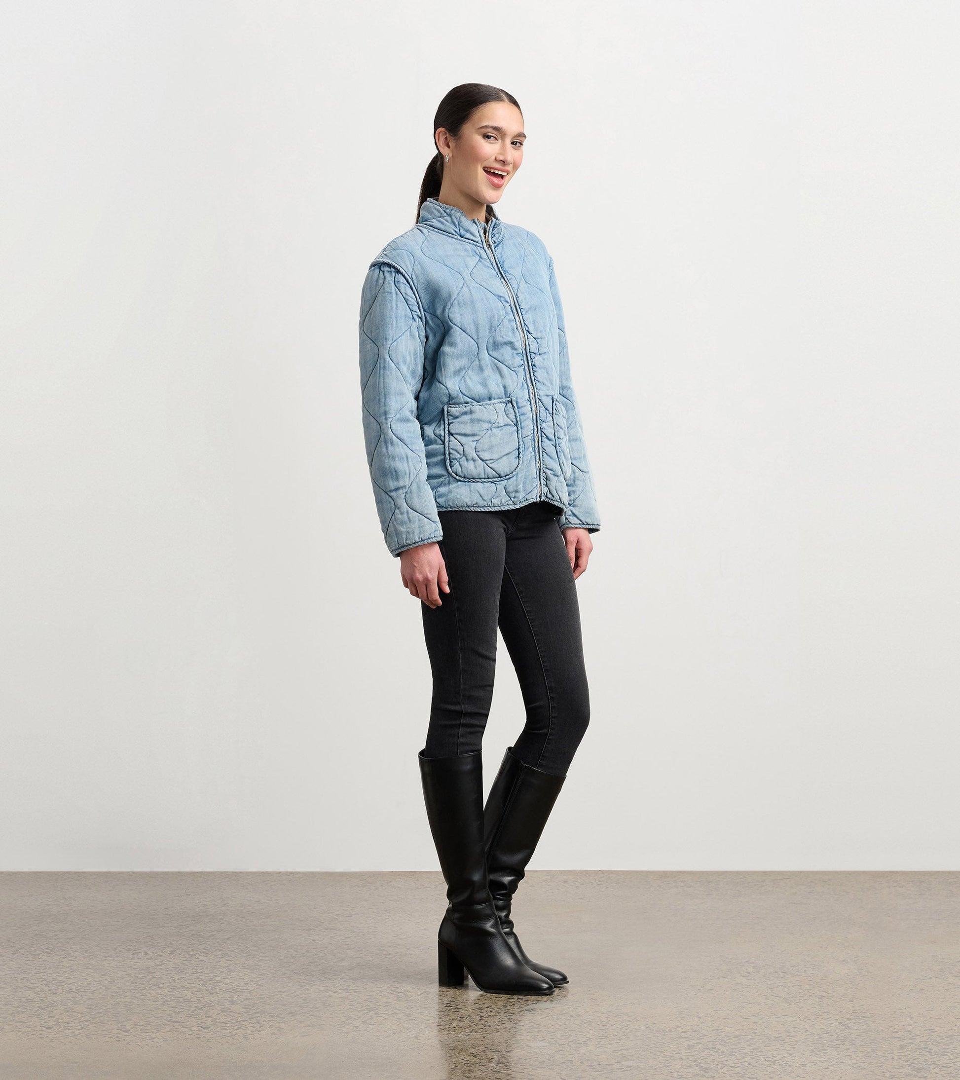 Quilted jacket in washed blue Tencel, featuring a zip front and two pockets, styled with black jeans and knee-high boots.