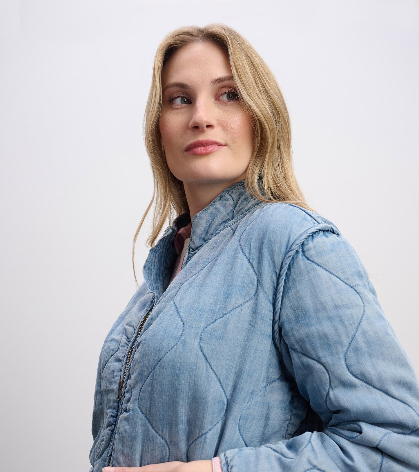 Quilted jacket in washed blue Tencel, featuring a high collar and zip closure, shown on a model from the side.