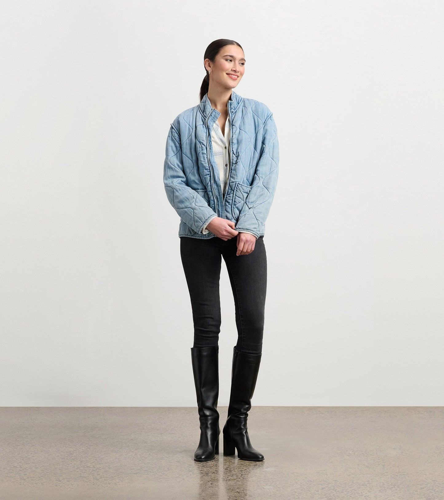 Quilted jacket in washed blue Tencel, featuring a stand collar and relaxed fit, styled with black jeans and knee-high boots.