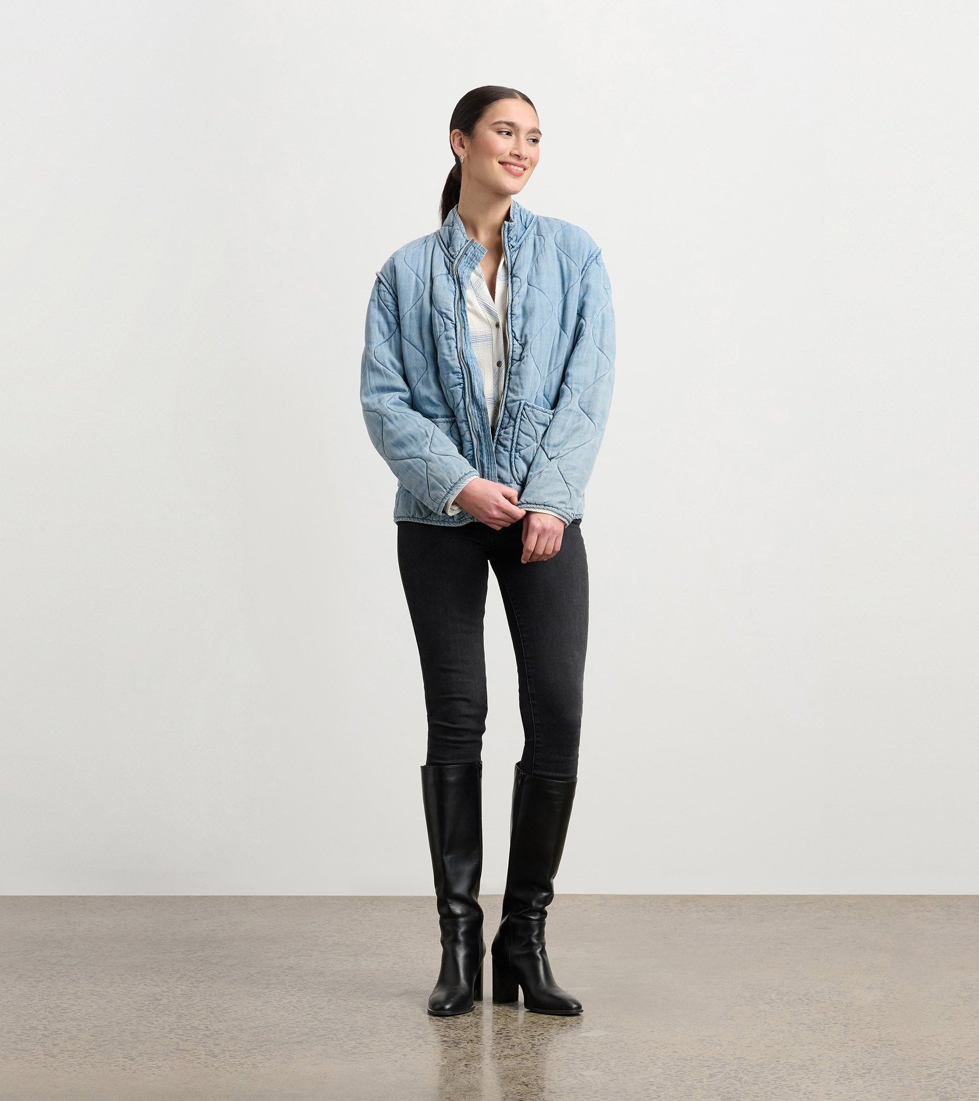 Quilted jacket in washed blue Tencel, featuring a stand collar and relaxed fit, styled with black jeans and knee-high boots.