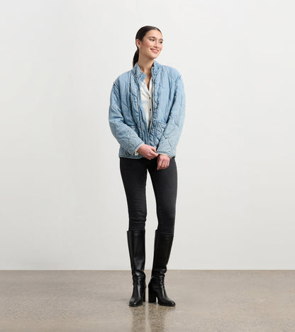 Quilted jacket in washed blue Tencel, featuring a stand collar and relaxed fit, styled with black jeans and knee-high boots.