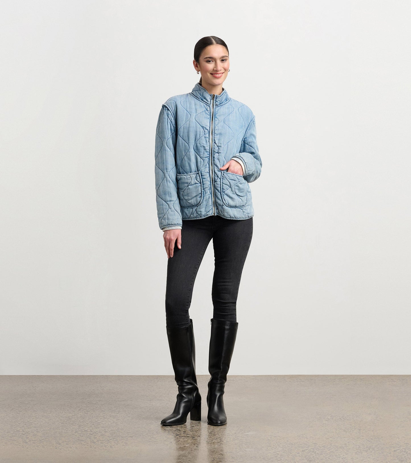 Quilted jacket in washed blue Tencel with a stand collar and front pockets, styled with black jeans and knee-high boots.