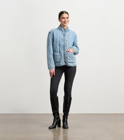 Quilted jacket in washed blue Tencel with a stand collar and front pockets, styled with black jeans and knee-high boots.