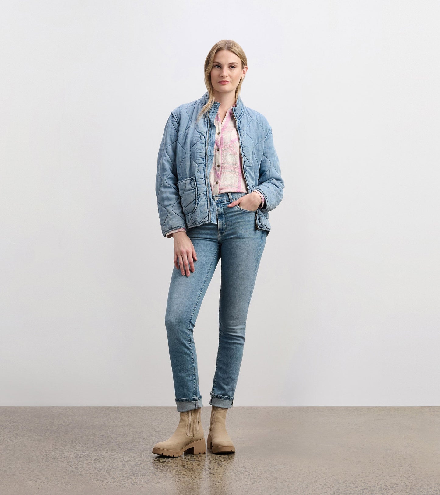 Quilted jacket in washed blue, featuring a zip front, side pockets, and a relaxed fit, paired with light jeans and boots.