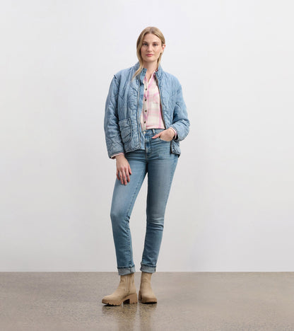 Quilted jacket in washed blue, featuring a zip front, side pockets, and a relaxed fit, paired with light jeans and boots.