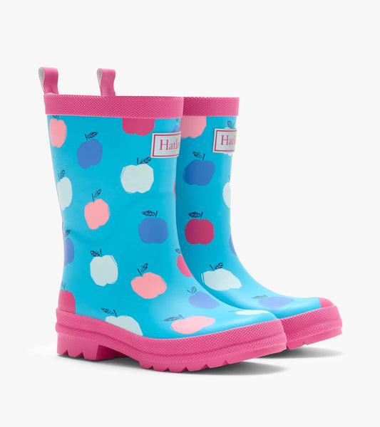 Pair of kids rain boots in blue with pink trim and multicolor apple print, angled front view