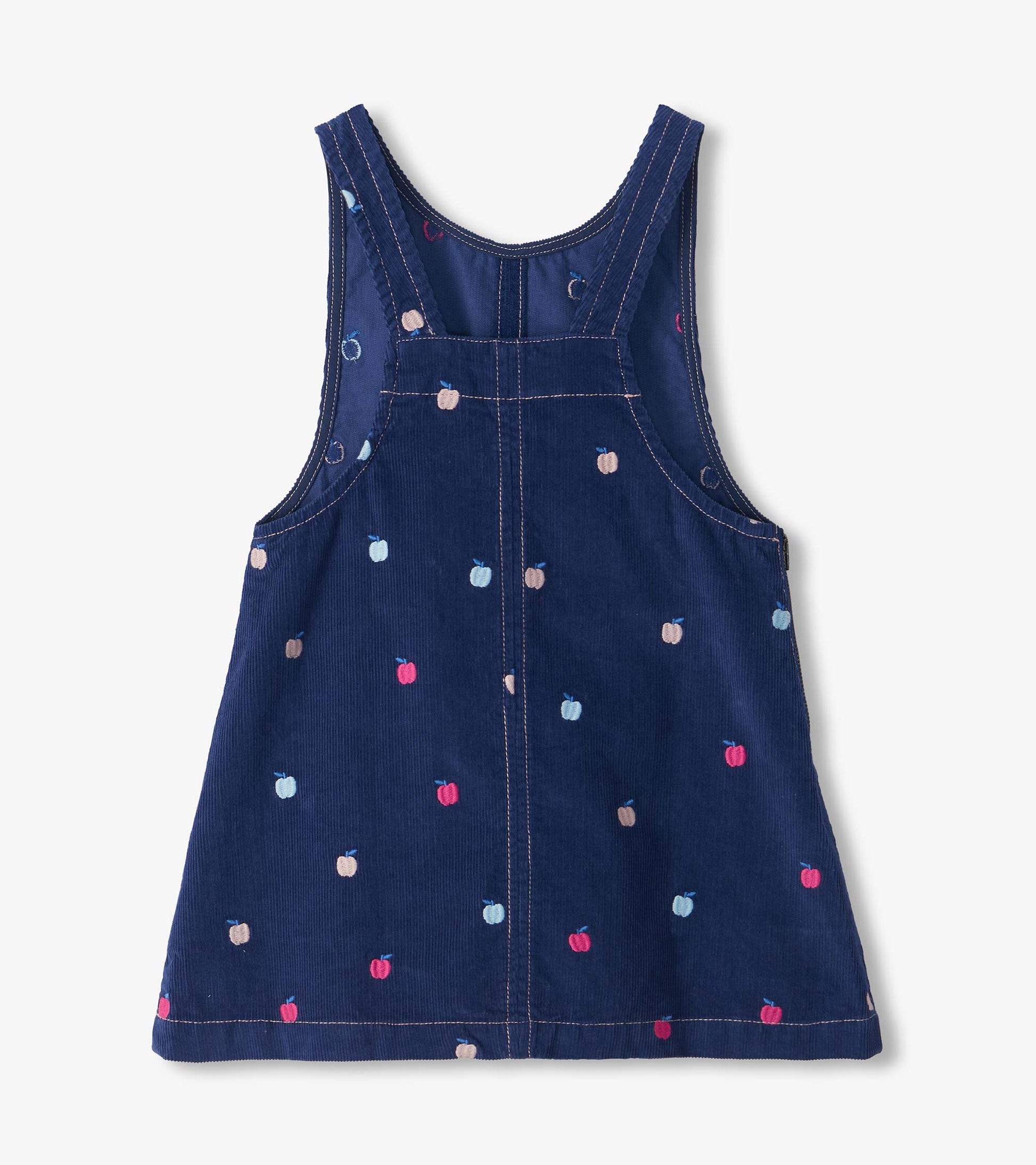 Back view of navy pinafore dress with cross-back straps and embroidered pink, blue, and beige apples