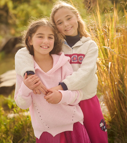 Girl wearing a light pink hooded pullover sweater with cream heart sleeves outdoors