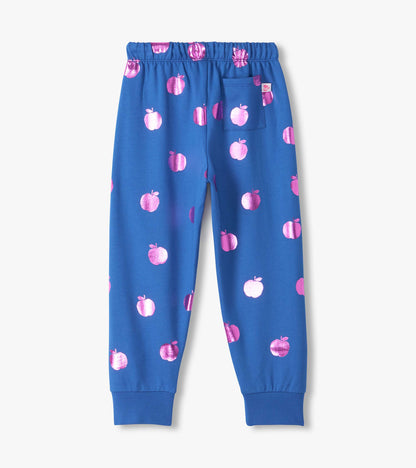 Back view of blue track pants with metallic pink apple print, cuffed ankles, and back patch pocket