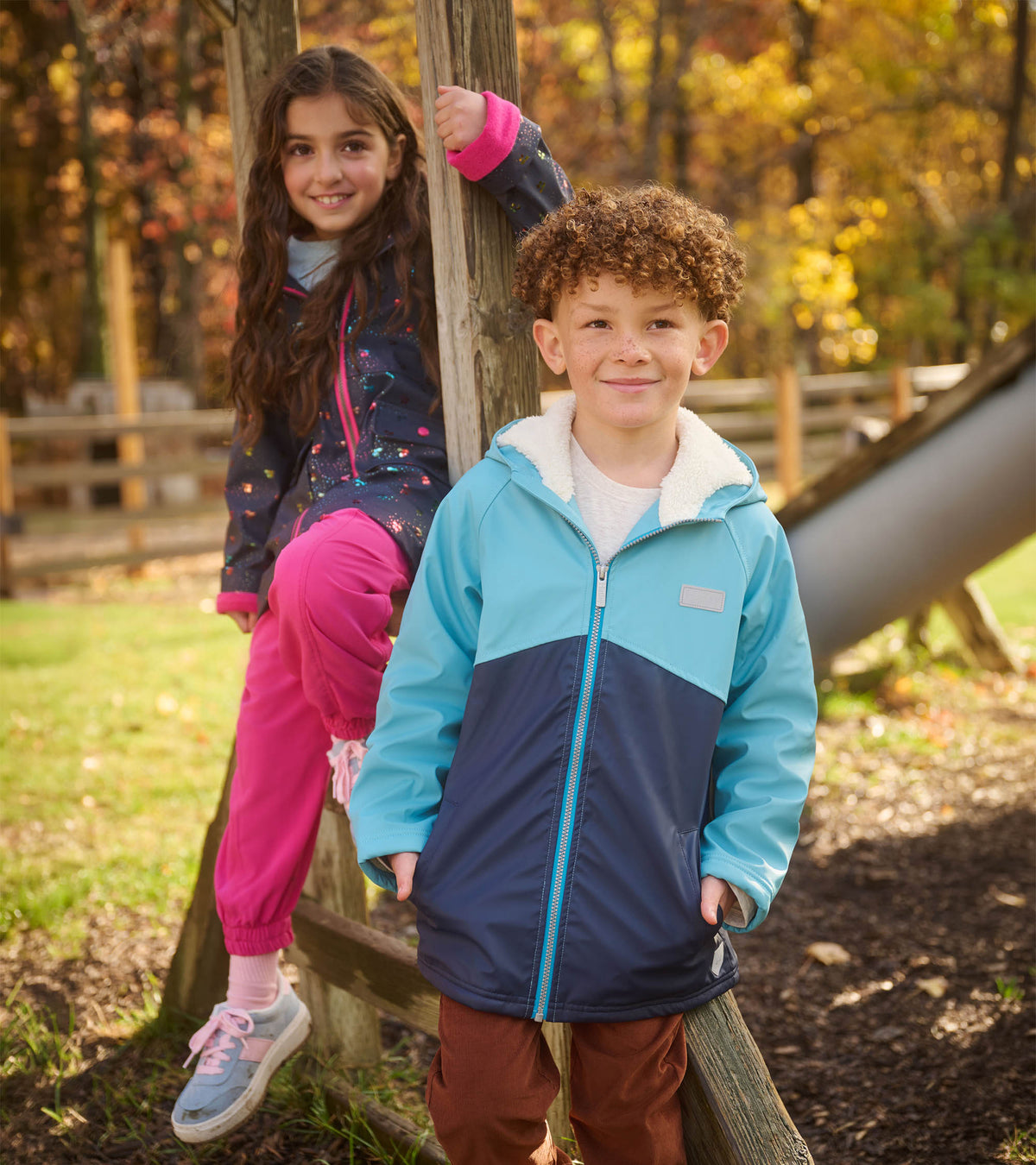 Boy wearing a blue colourblock sherpa-lined raincoat outdoors near wooden play equipment