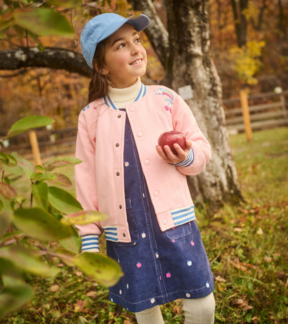 Girl wearing pink varsity bomber jacket with blue striped trim and embroidered motifs outdoors