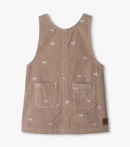 Front view of taupe pinafore dress with pink and white bow embroidery and two front patch pockets