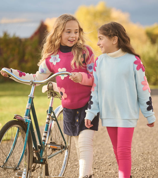 Girl wearing a cool blue slouchy pullover with pink and navy flower appliqués down the raglan sleeves