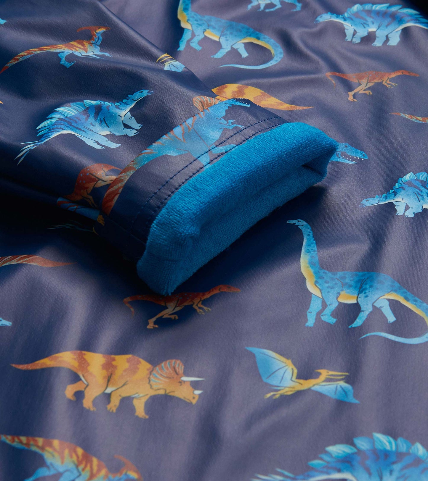 Close-up of rain coat cuff with blue lining and colorful dinosaur print on dark blue background