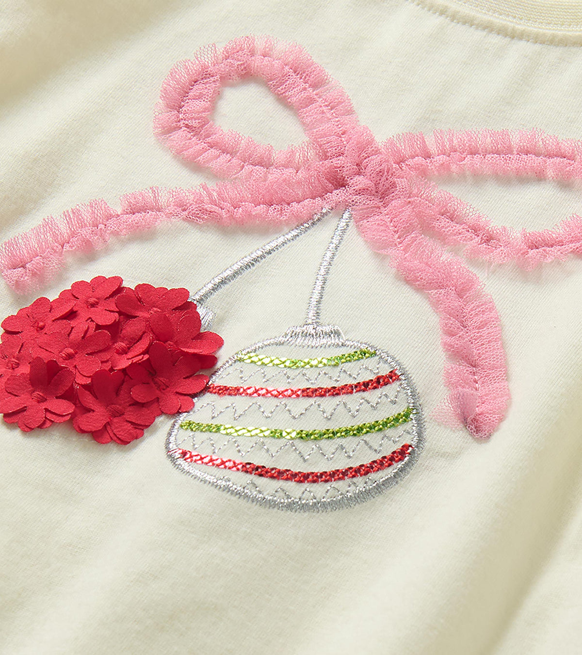 Close-up of pink bow and ornament chest graphic with red floral appliqué and embroidered details