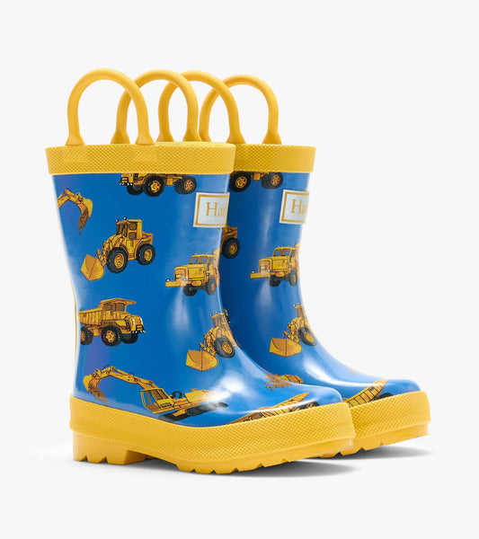 Pair of blue kids rain boots with yellow handles and yellow construction truck print, front angled view