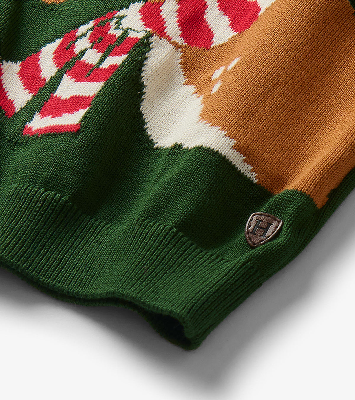 Close-up of the sweater hem showing the reindeer pattern, red and white striped scarf, and small logo patch
