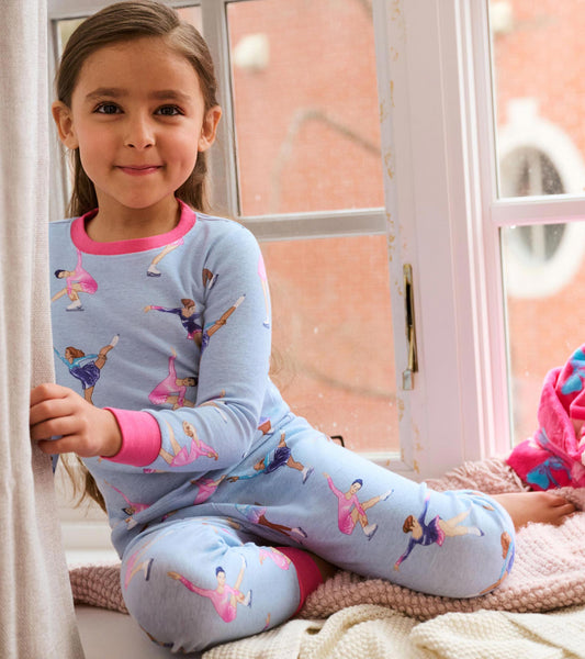 Girl wearing light blue figure skater pajamas with pink trim, seated by a window