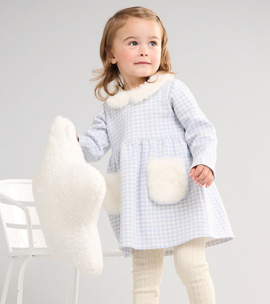 Toddler girl wearing a light blue and white houndstooth dress with a white fluffy collar and patch pockets